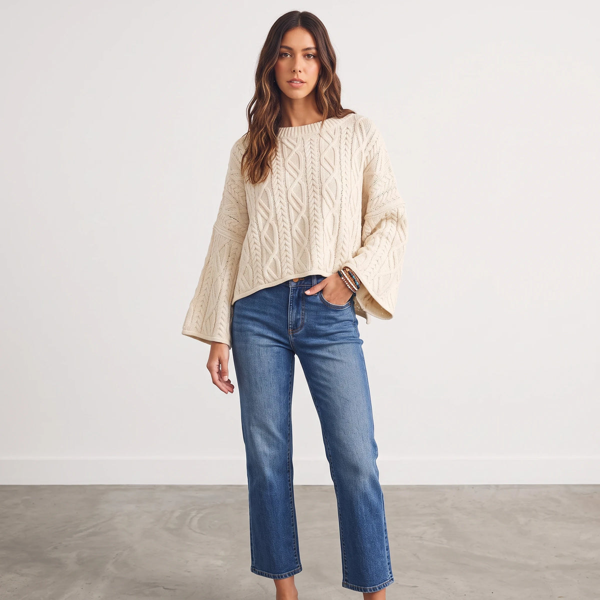 Model wearing Apricot Lane Duluth oversized cream cable-knit sweater with flared sleeves and blue straight-leg jeans.