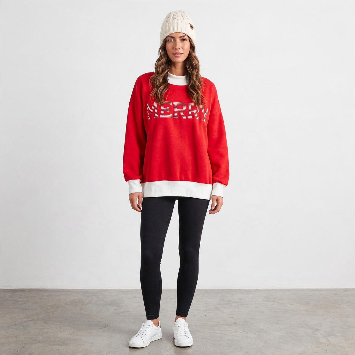 Apricot Lane Duluth red oversized Christmas mock neck top with MERRY text, worn with black leggings and white beanie.