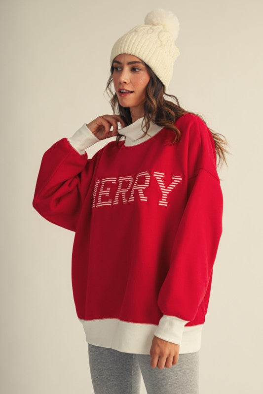 Apricot Lane Duluth oversized red Christmas top with mock neck, white ribbed trim, and Merry graphic on a model.