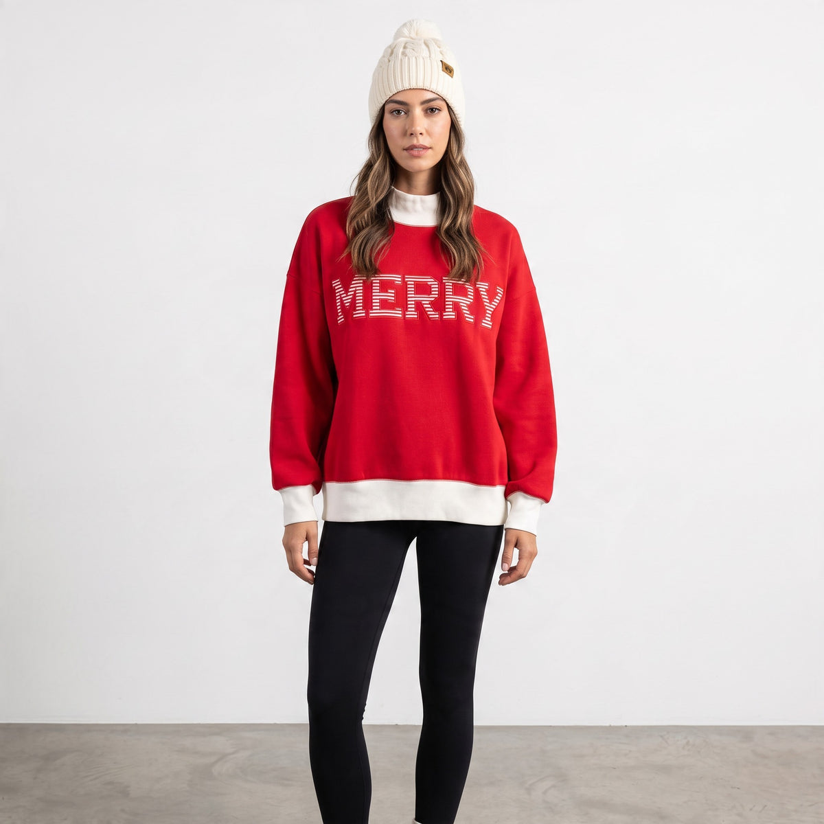 Model wearing Apricot Lane Duluth red oversized Merry Christmas mock neck top with white ribbed trim and beanie