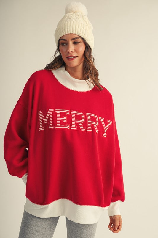 Apricot Lane Duluth red oversized mock neck Christmas top with MERRY text and white pom-pom beanie on a model