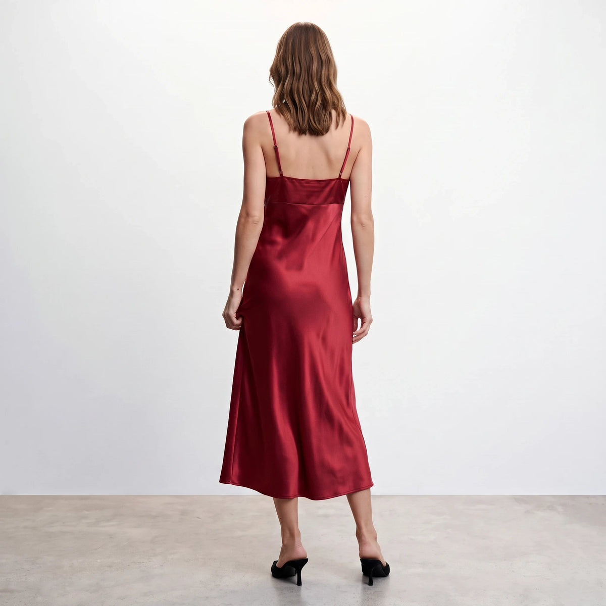 Back view of Apricot Lane Duluth red satin midi slip dress with thin cami straps on a model against a white wall