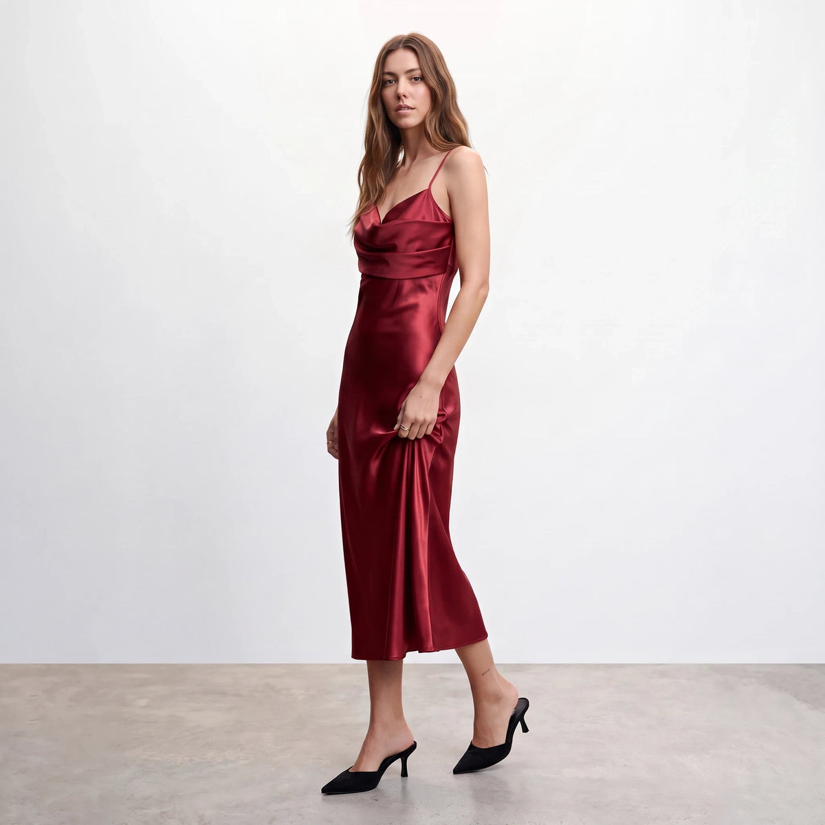 Model wearing Apricot Lane Duluth red satin midi dress with asymmetrical cowl neck and cami straps against white wall