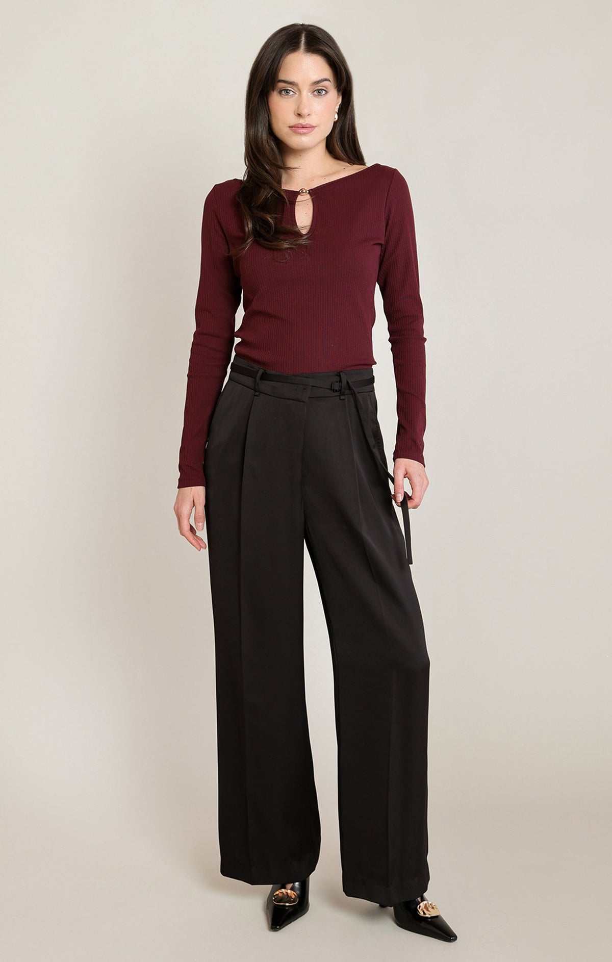 Model wearing Apricot Lane Duluth black satin belted wide-leg pants with a burgundy long-sleeve top and black heels.