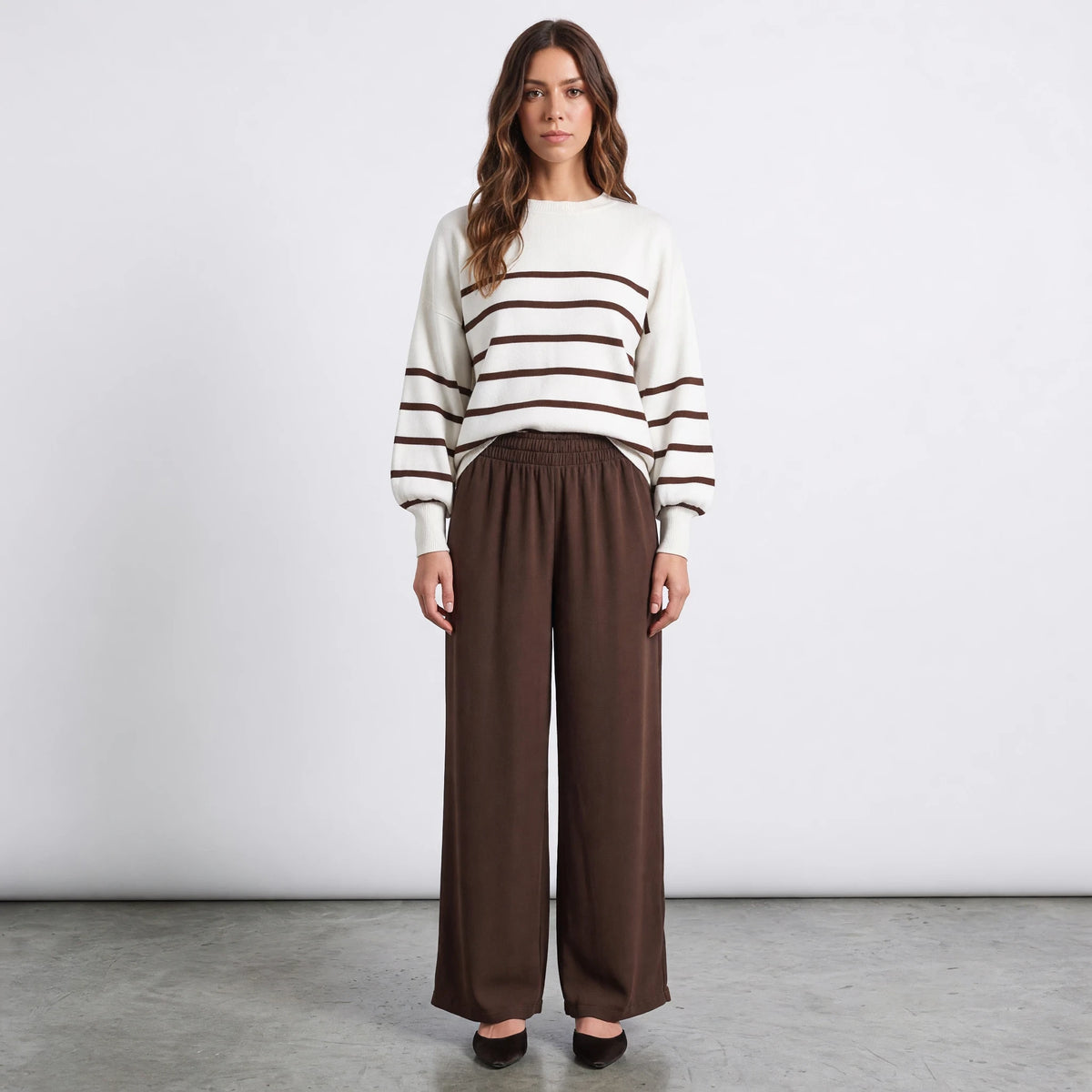 Model wearing Apricot Lane Duluth striped balloon sleeve sweater with brown wide-leg trousers and black pointed heels.