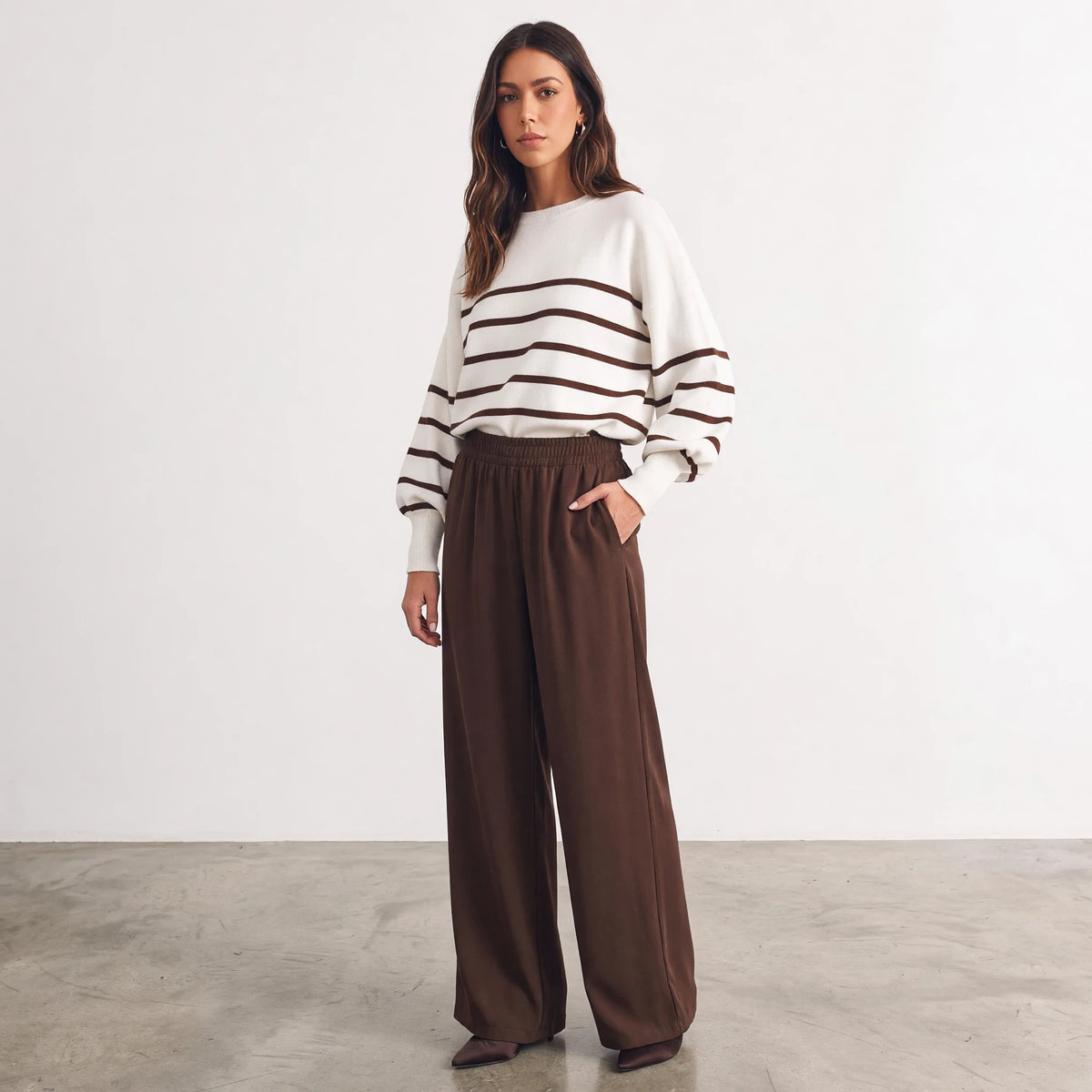 Model wearing Apricot Lane Duluth striped balloon sleeve sweater with brown wide-leg trousers in a studio setting.
