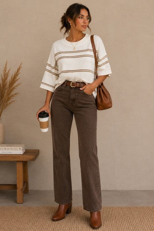 Apricot Lane Duluth model wearing a white short-sleeve knit sweater with brown stripes and dark brown denim jeans.