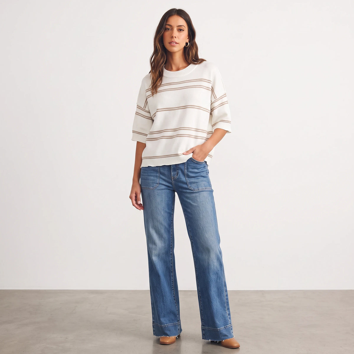 Apricot Lane Duluth model wearing a cream and tan striped short-sleeve knit sweater with wide-leg blue jeans
