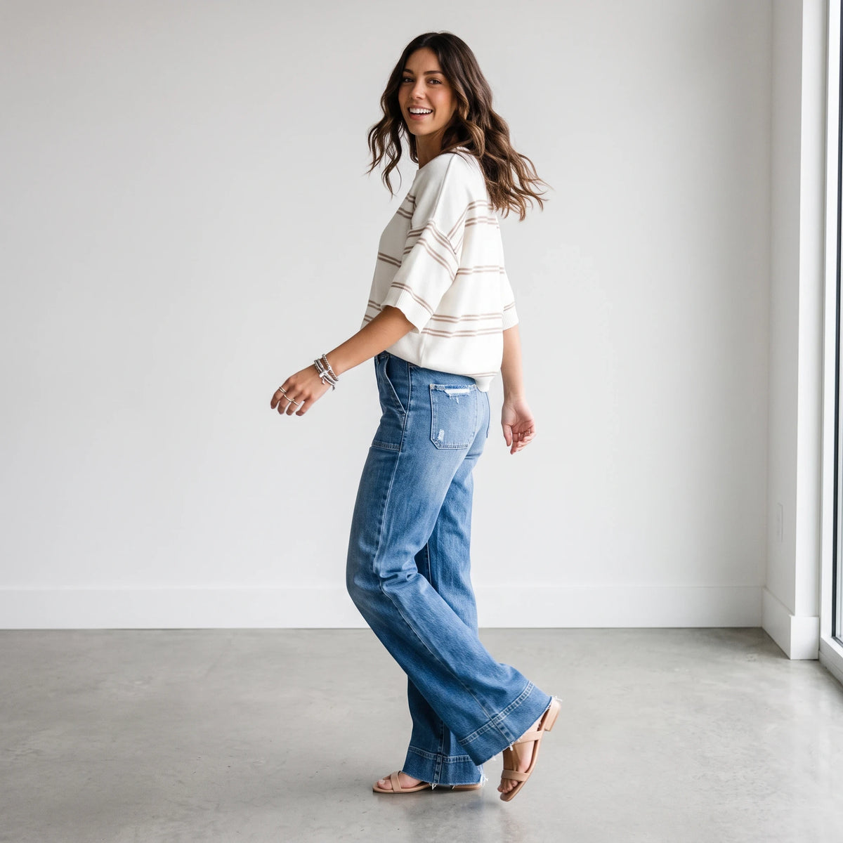 Apricot Lane Duluth model wearing a cream and tan striped short-sleeve knit sweater with wide-leg blue denim jeans.