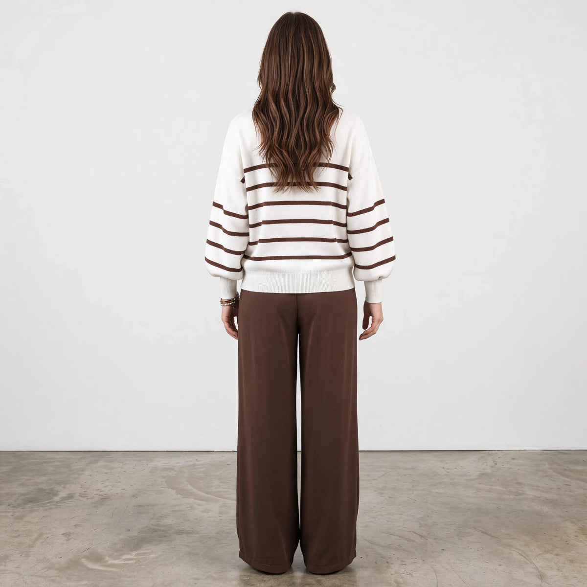 Back view of a woman wearing an Apricot Lane Duluth striped balloon sleeve sweater with brown trousers.