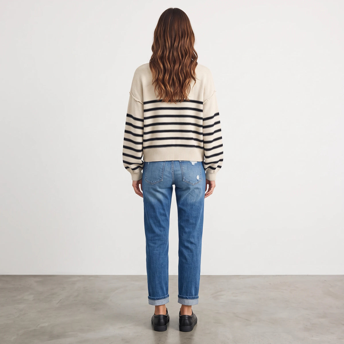 Back view of a woman wearing the Apricot Lane Duluth striped sweater with blue jeans and black loafers.