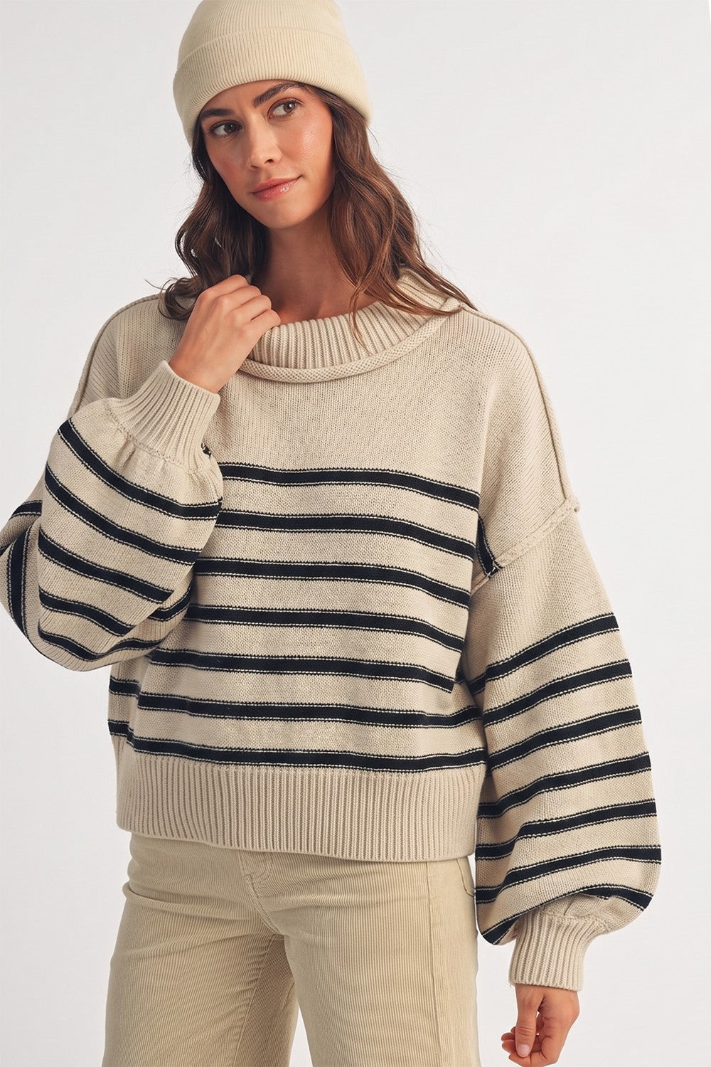 Model wearing an Apricot Lane Duluth beige and black striped cotton-blend sweater with a matching beanie.