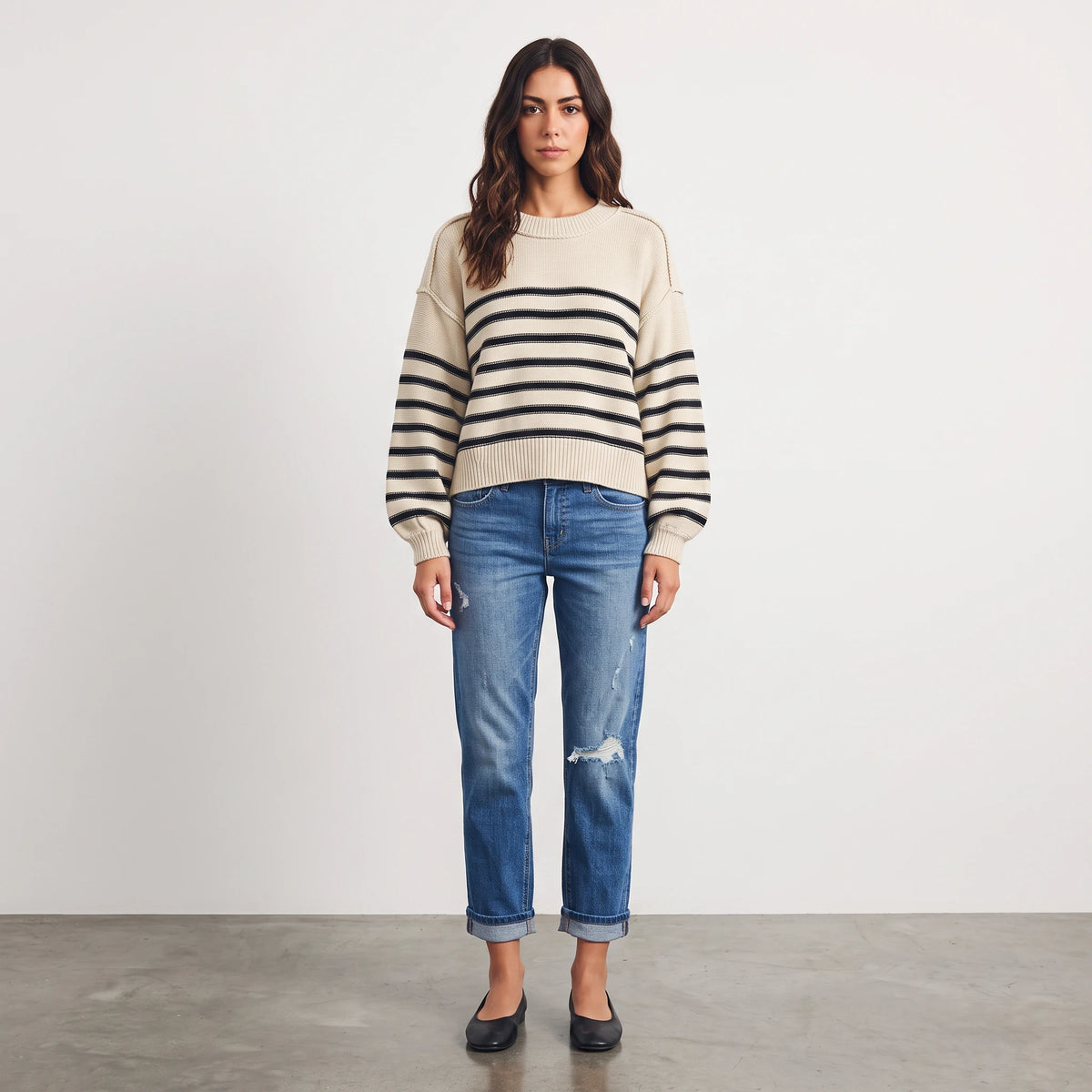 Model wearing Apricot Lane Duluth Fireside Lane Stripe Sweater in cream with black stripes and blue distressed jeans.