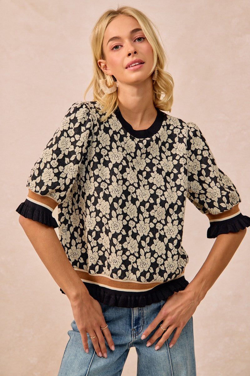 Woman wearing a black floral blouse with ruffled sleeves against a beige background