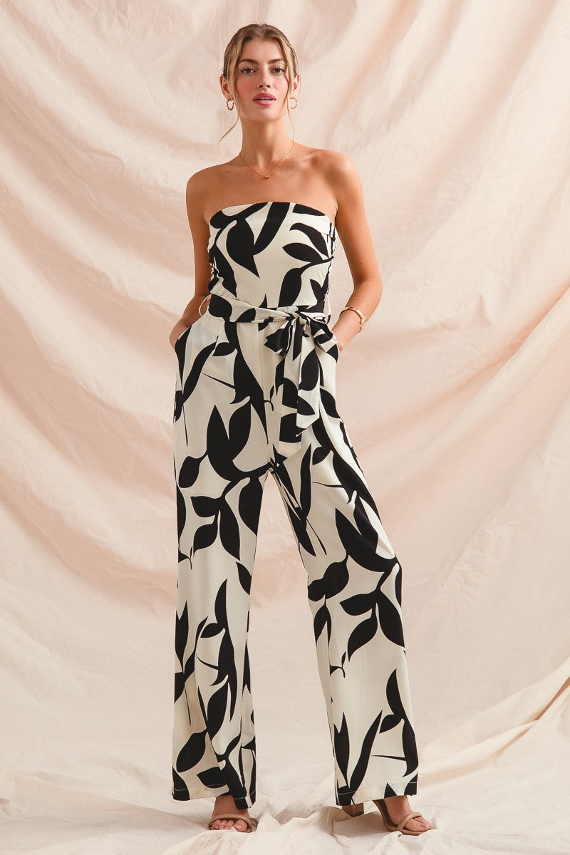 Woman wearing a strapless black and white leaf-patterned jumpsuit against a beige background