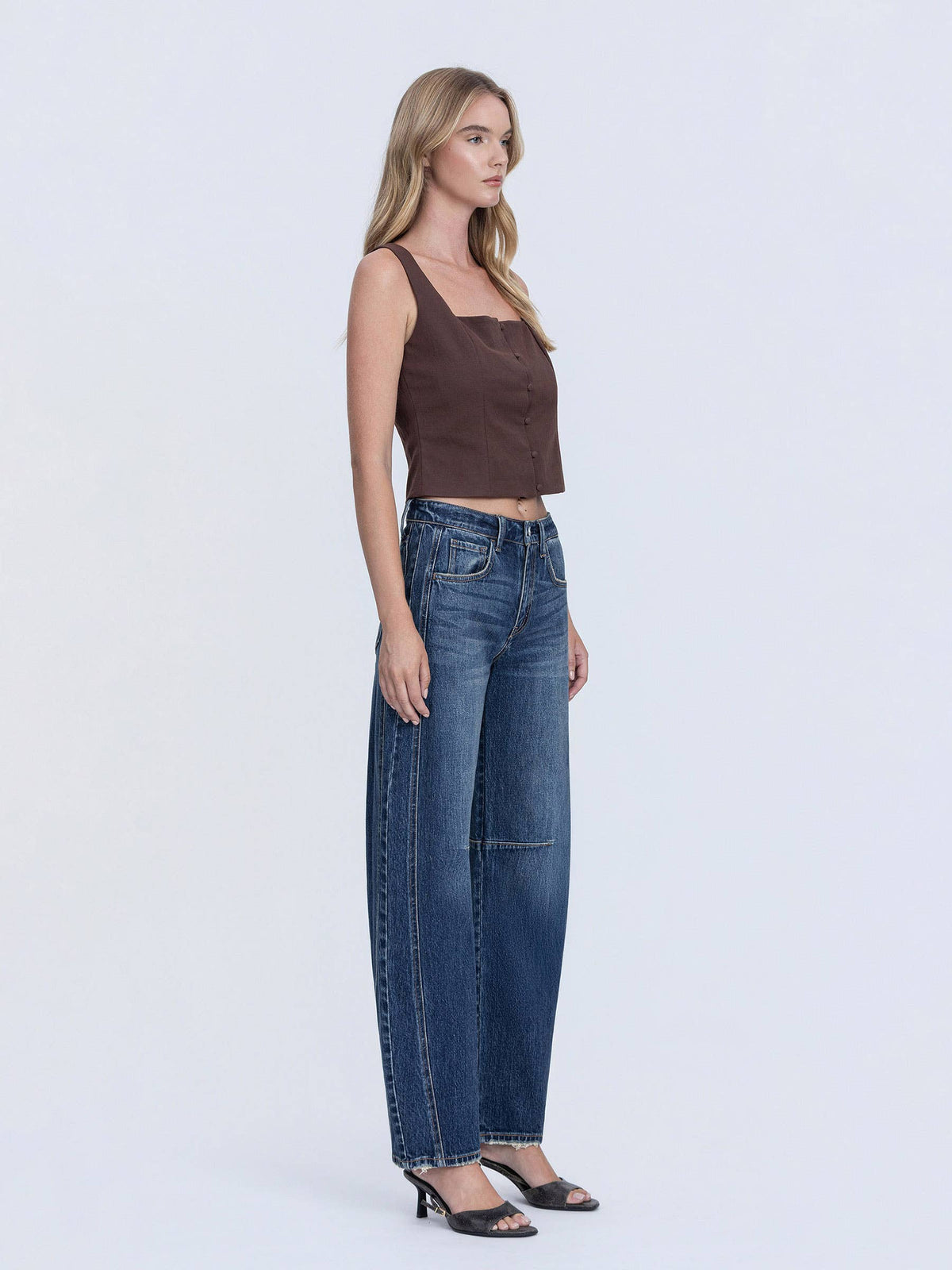 Woman wearing a brown top and blue jeans on a white background