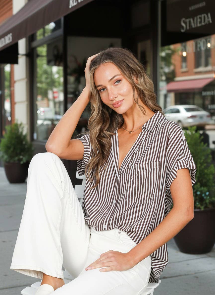 Woman sitting on a bench in an urban setting wearing a striped shirt and white pants.