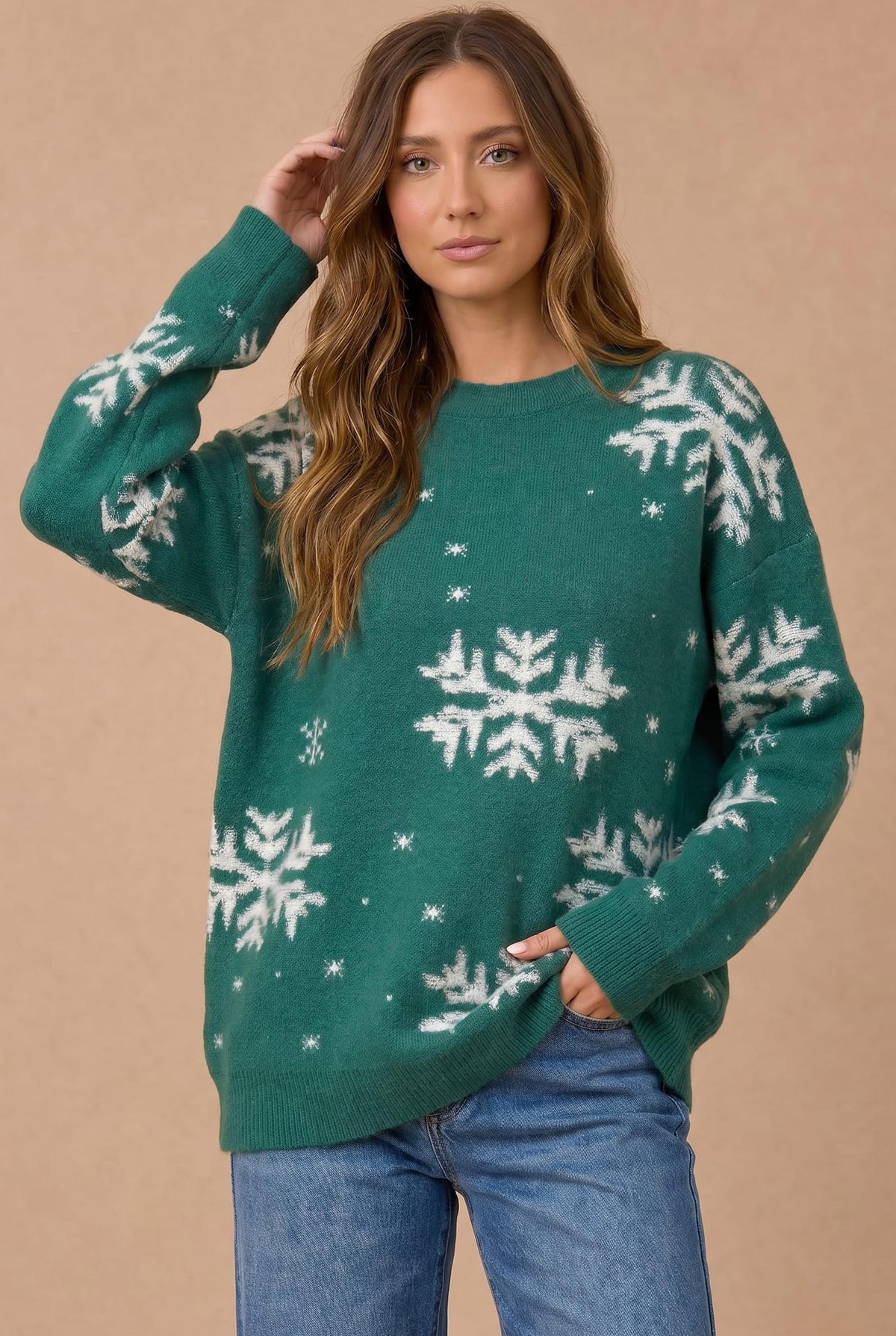 A woman wearing a green crewneck sweater with white snowflake patterns, paired with blue jeans, standing against a solid beige background.