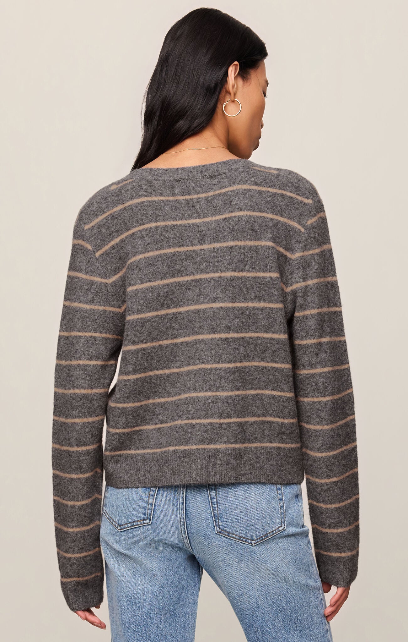 Person wearing a gray and beige striped sweater with blue jeans on a beige background