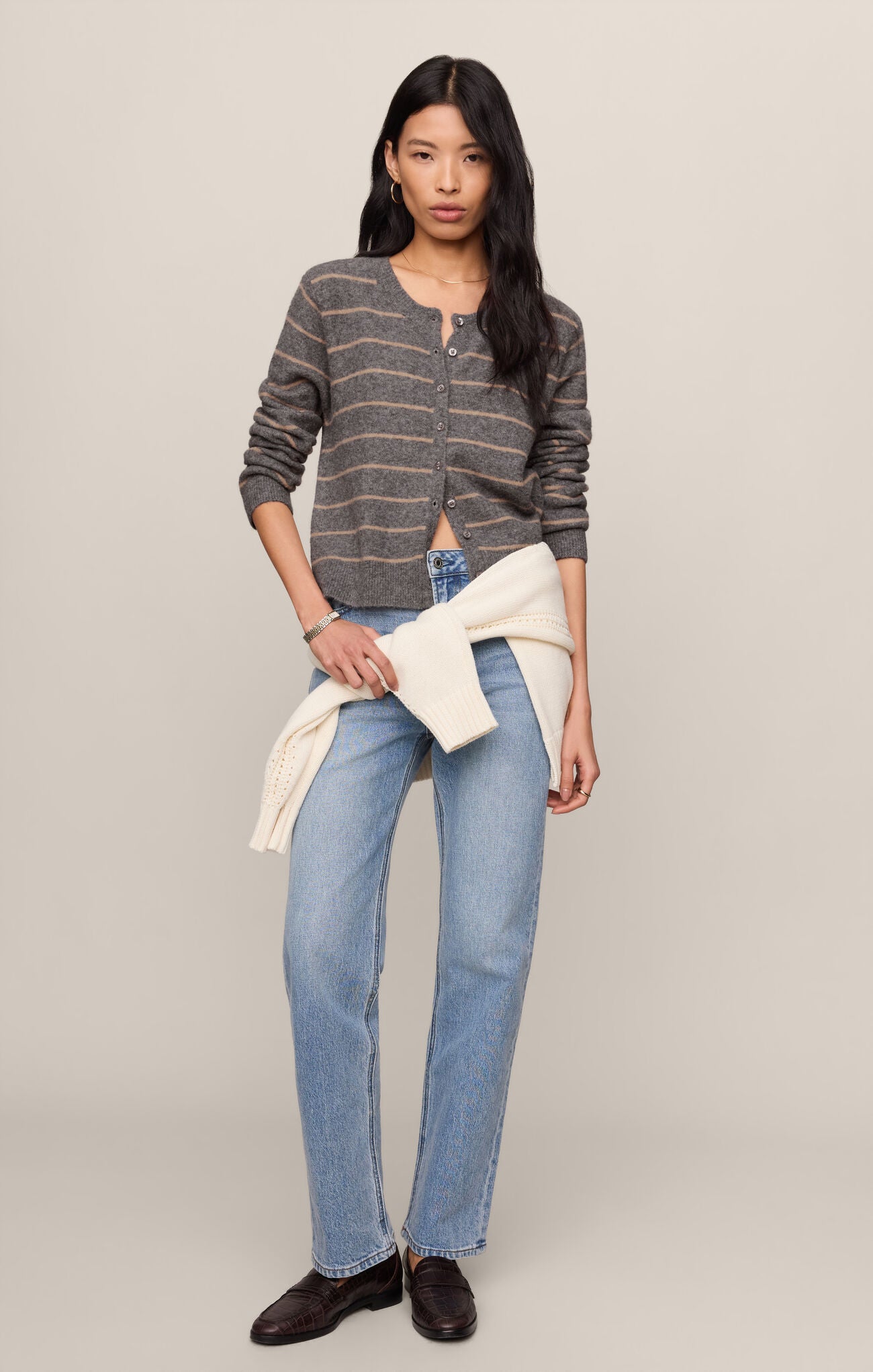 Woman wearing a striped sweater, jeans, and a white jacket on a plain background
