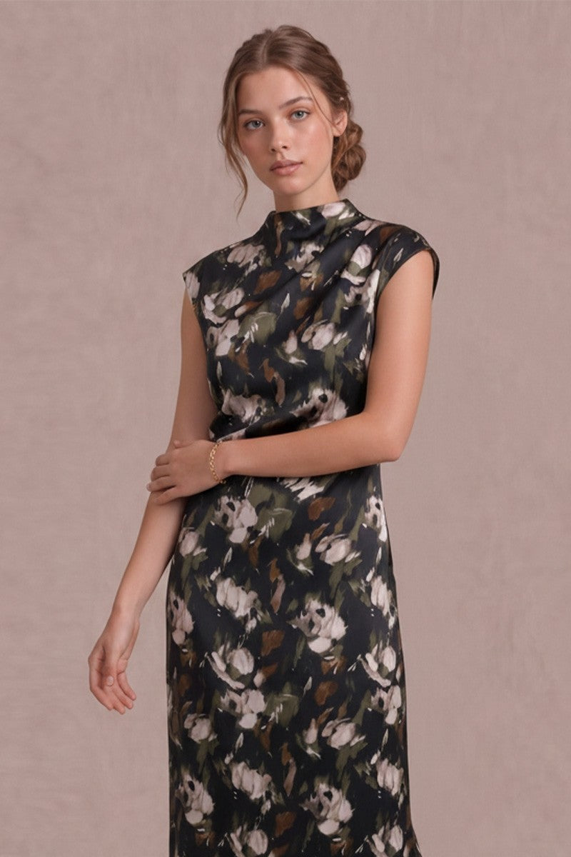 A woman modeling a sleeveless high-neck dress with a dark floral print in white, beige, and brown tones, set against a solid dusty pink studio background.
