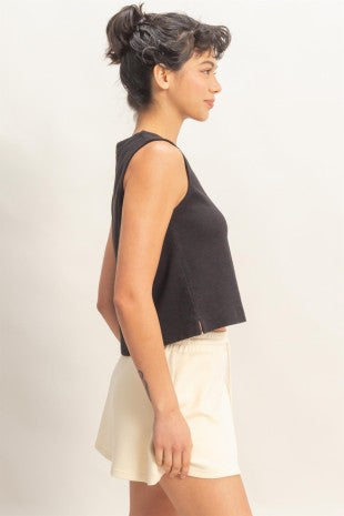Woman wearing a black sleeveless top and white shorts on a plain background