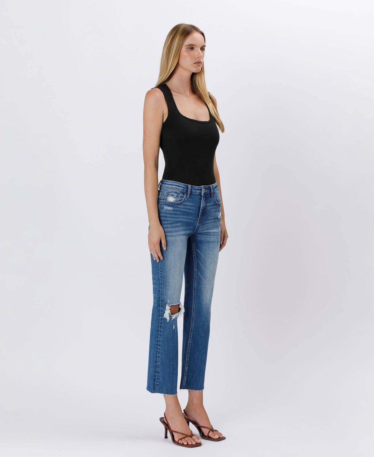 Woman wearing a black tank top and blue jeans on a white background