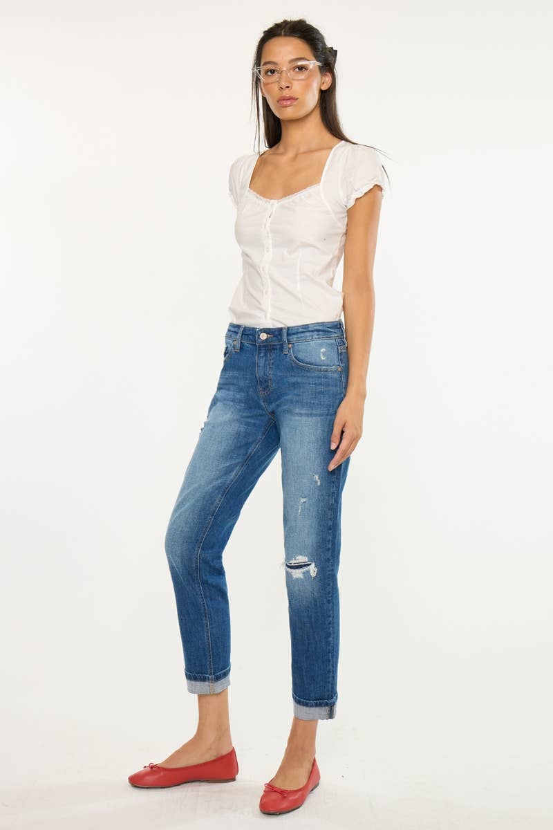 A woman modeling a white short-sleeve top and distressed blue cropped jeans with rolled cuffs, paired with red flats, against a plain white studio background.