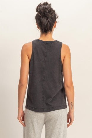Person wearing a black sleeveless top and gray pants against a plain background
