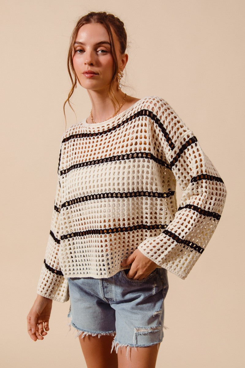 Woman wearing a white crochet sweater with black stripes and denim shorts on a beige background