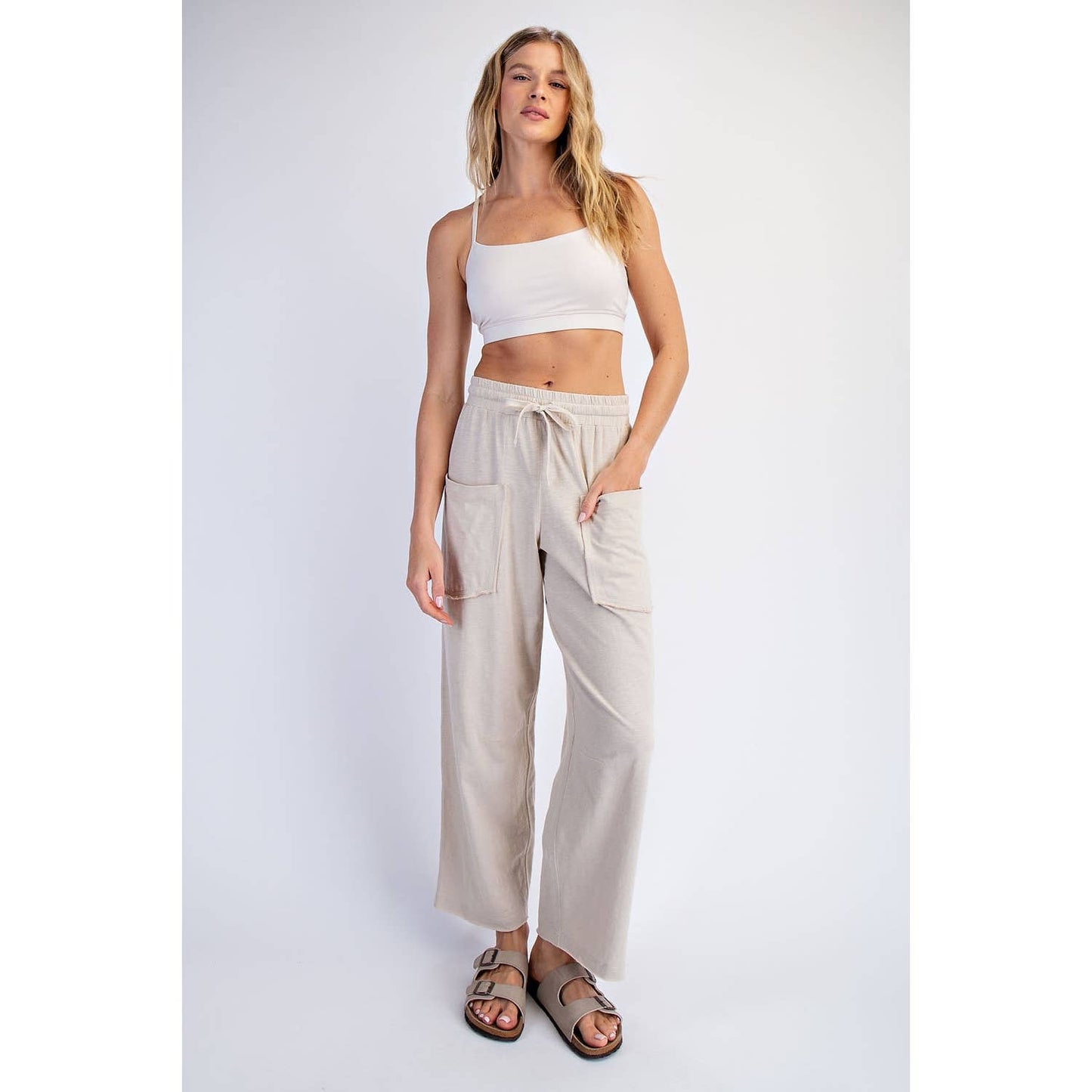 Woman wearing a white top and beige pants on a plain background