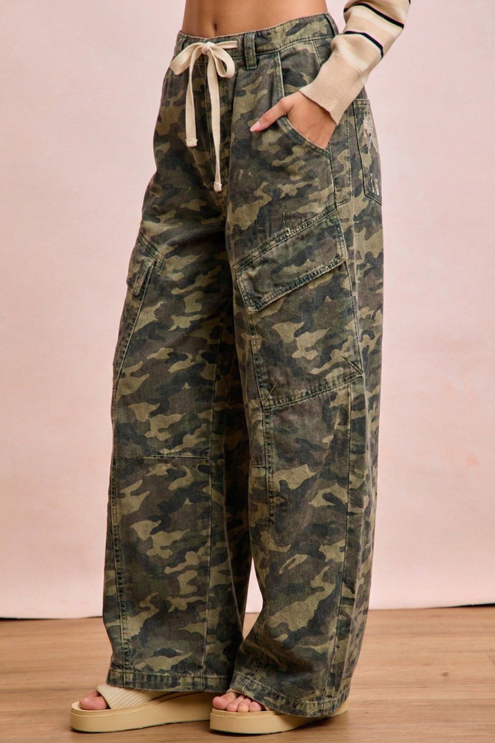 Camouflage pants worn by a person on a wooden floor with a pink background