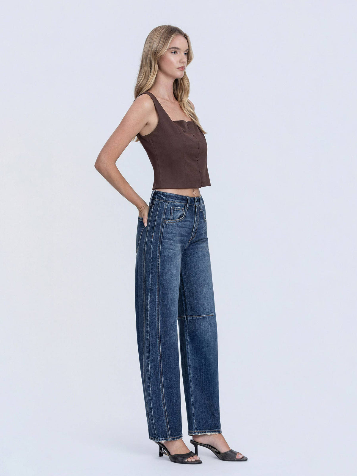 Woman wearing a brown tank top and blue jeans on a white background