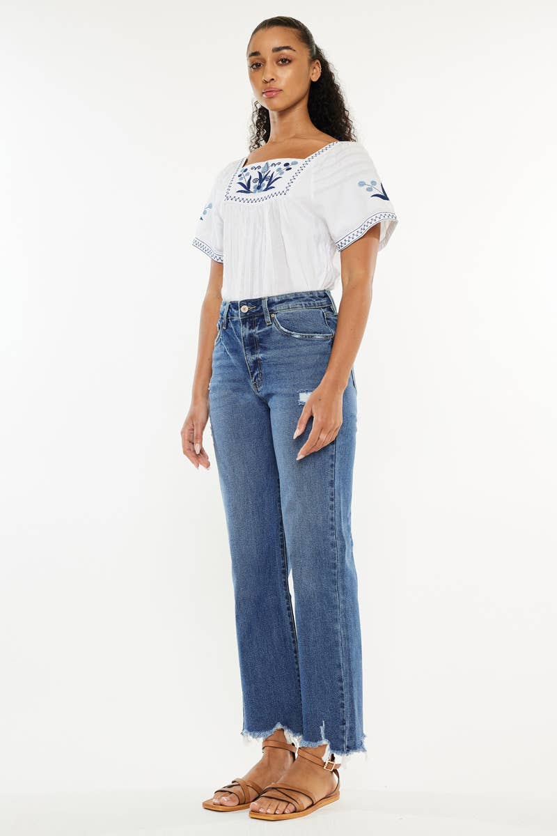 Woman wearing a white blouse with floral embroidery and blue jeans on a white background