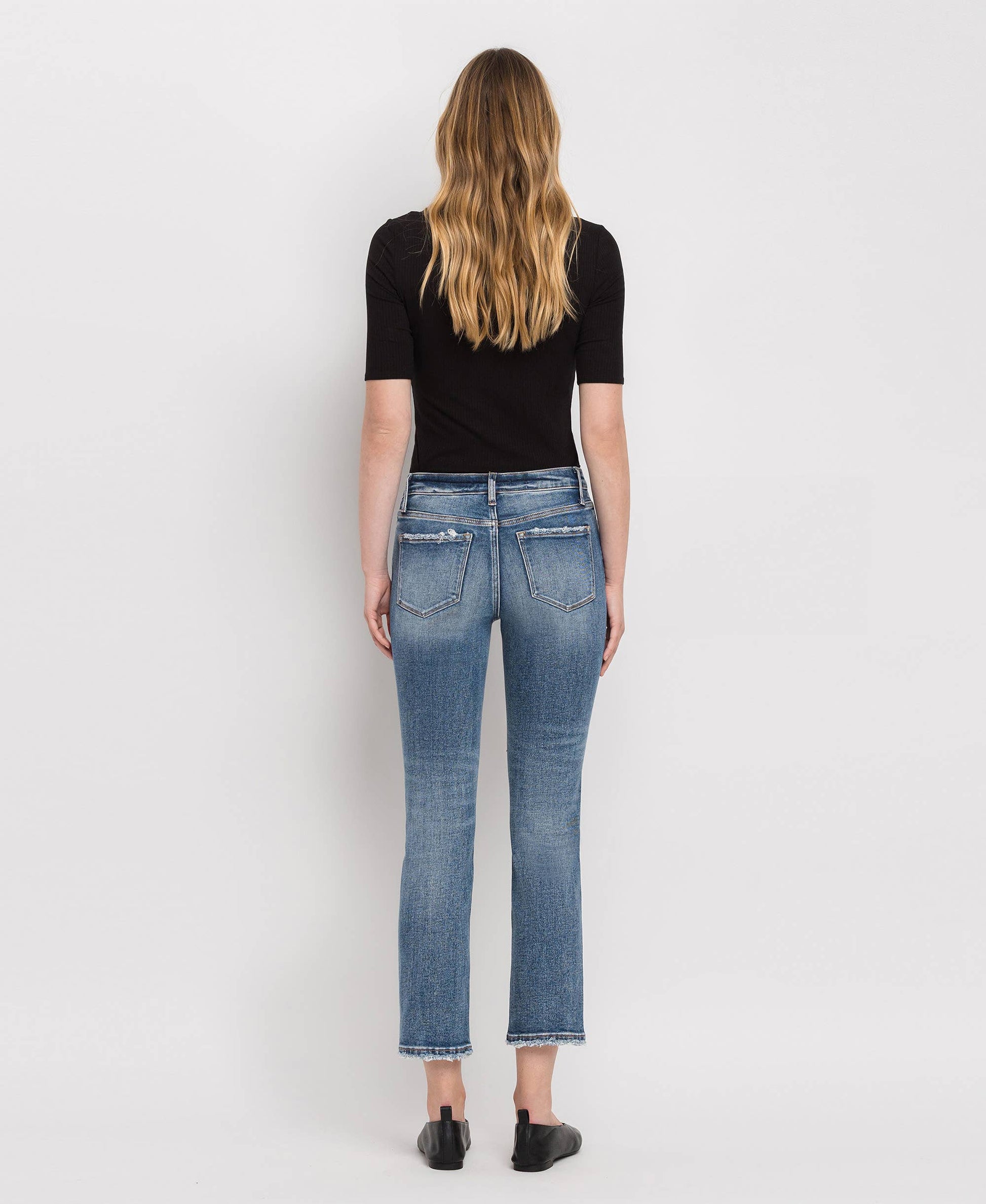 Person wearing blue jeans and a black top on a white background