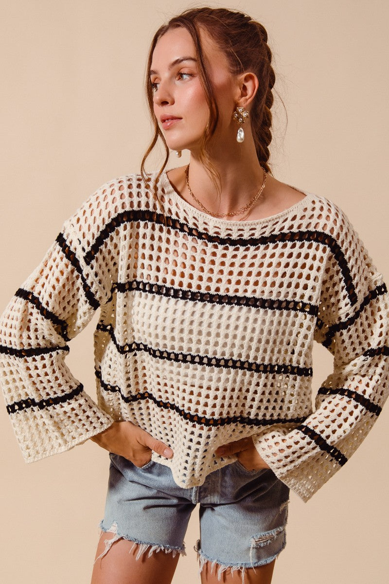 Woman wearing a beige and black patterned sweater with denim shorts on a beige background