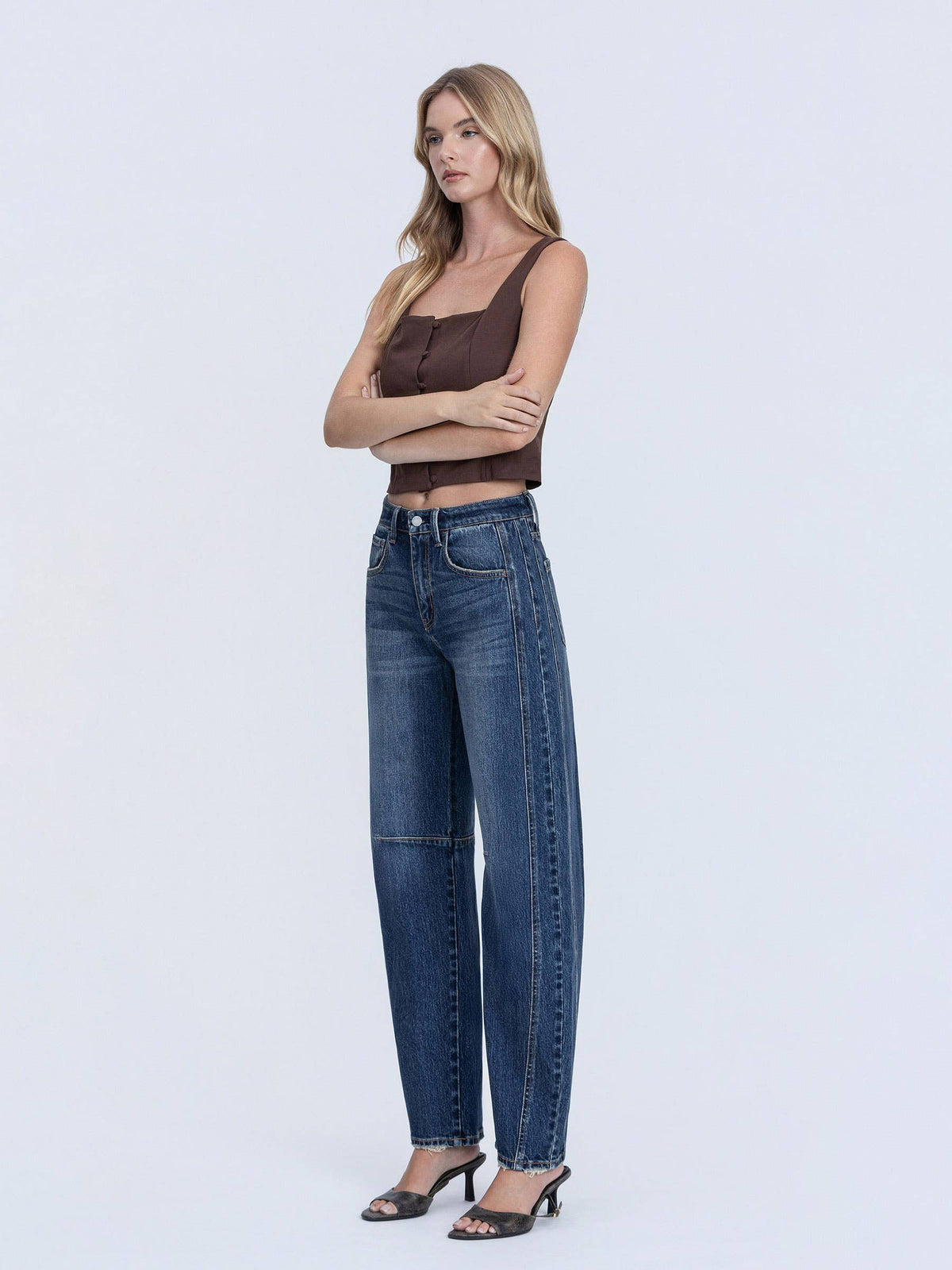 Woman wearing blue jeans and a brown top on a white background