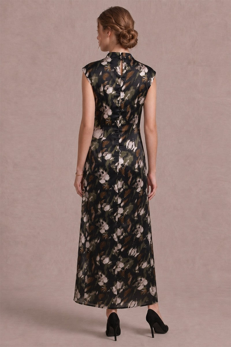 A woman viewed from the back wearing a sleeveless black maxi dress with a white and beige floral print, paired with black heels, against a solid mauve background.