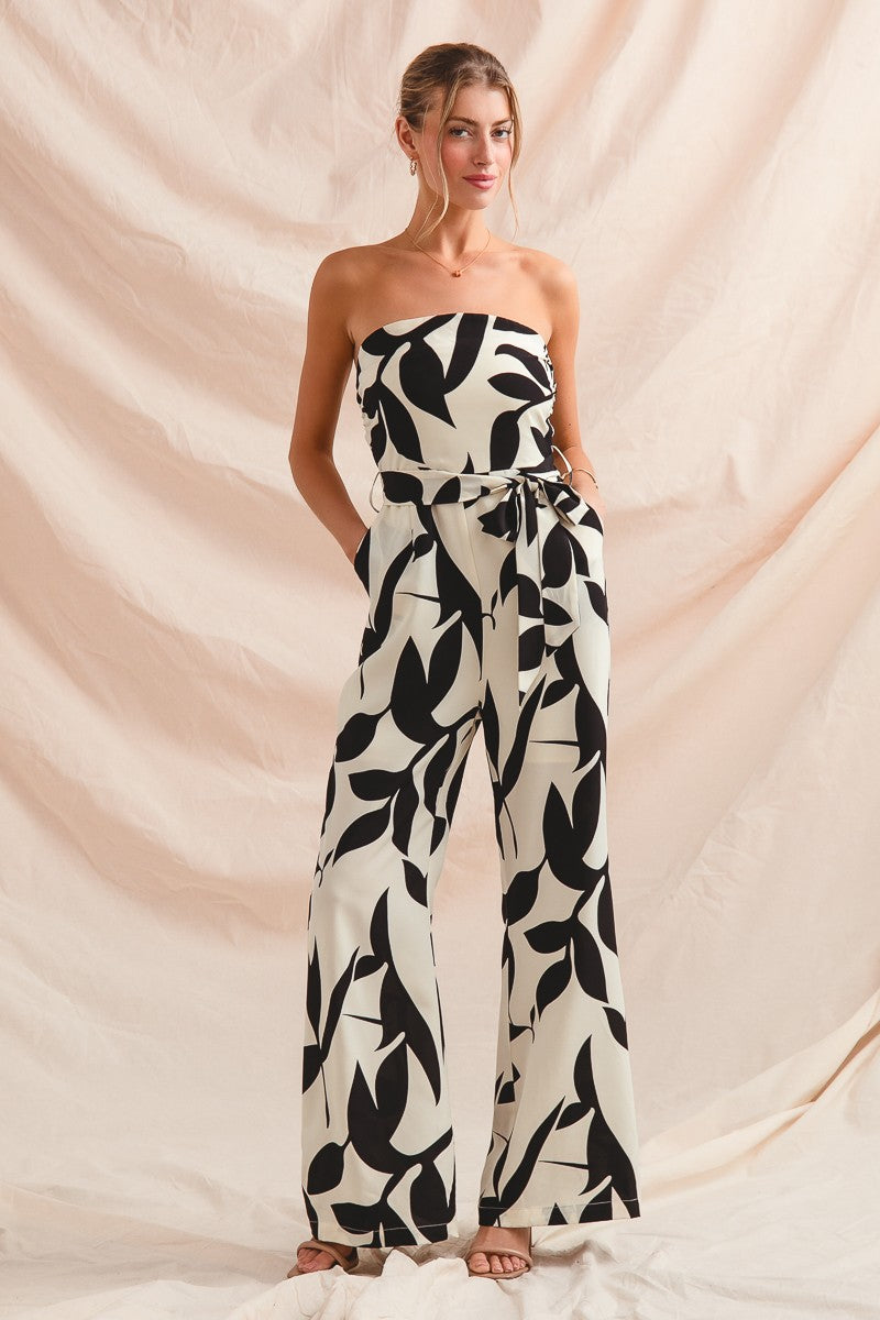Woman wearing a strapless black and white leaf-patterned jumpsuit against a beige backdrop