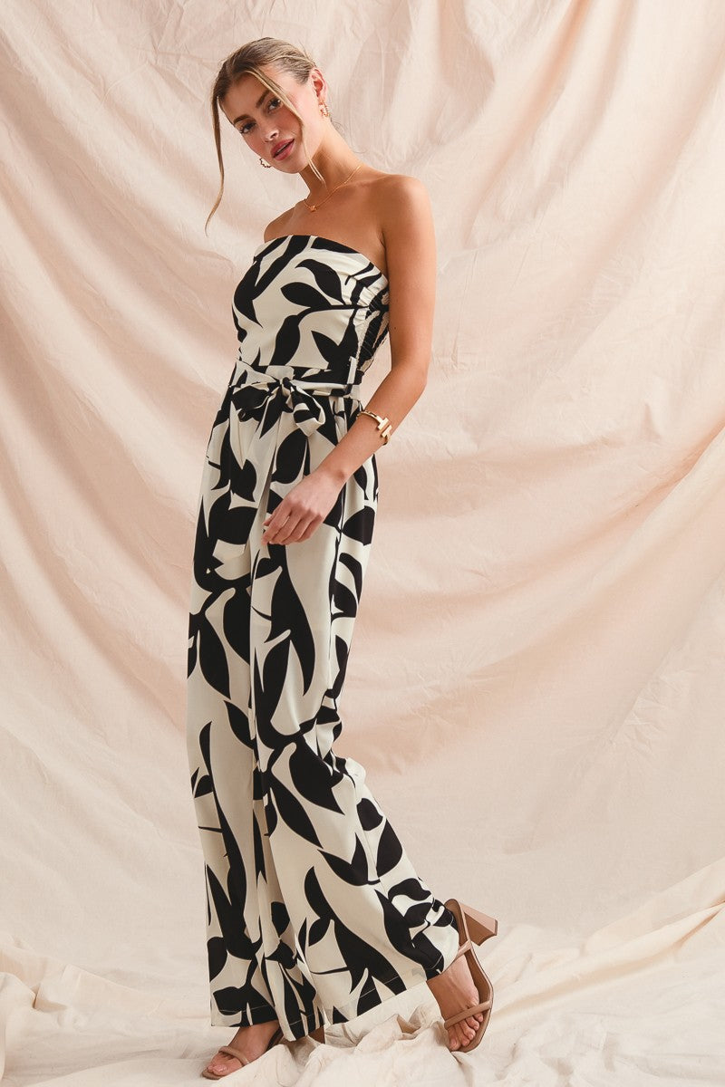 Woman wearing a strapless black and white patterned jumpsuit against a beige background