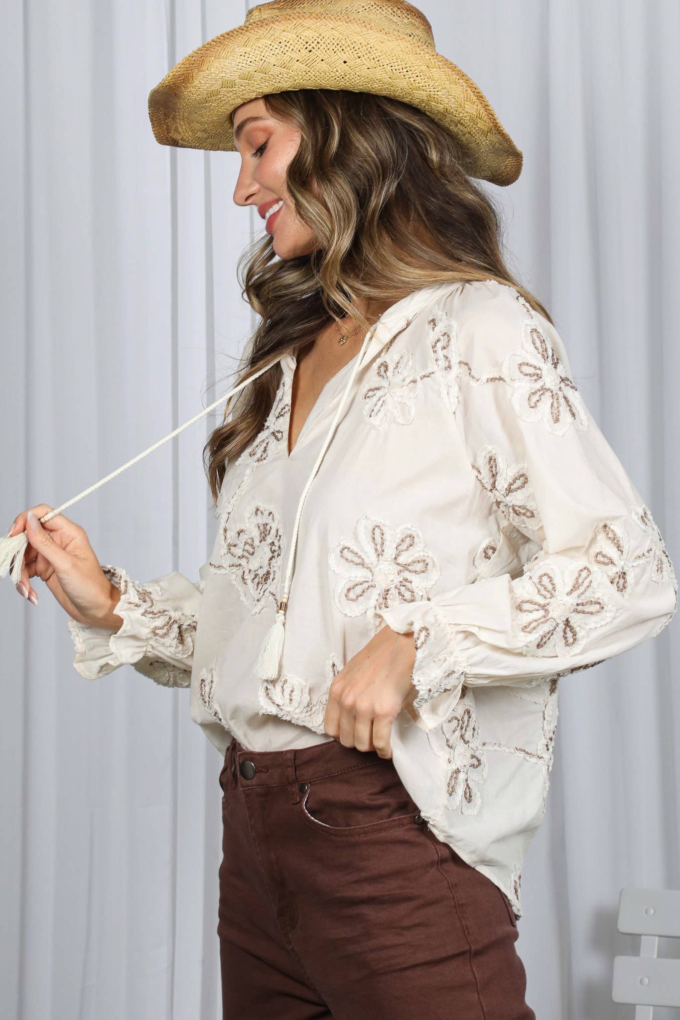 Woman wearing a white embroidered blouse and brown hat against a light background