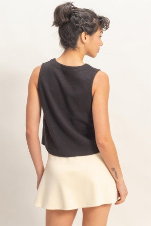 Woman wearing a black sleeveless top and cream skirt on a plain background