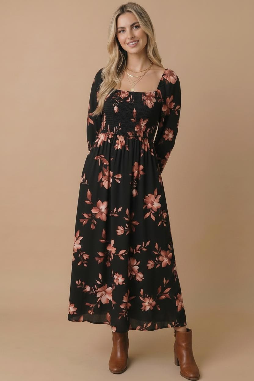 A woman modeling a long-sleeve black maxi dress with a dusty rose floral print, paired with brown ankle boots, against a solid beige studio background.
