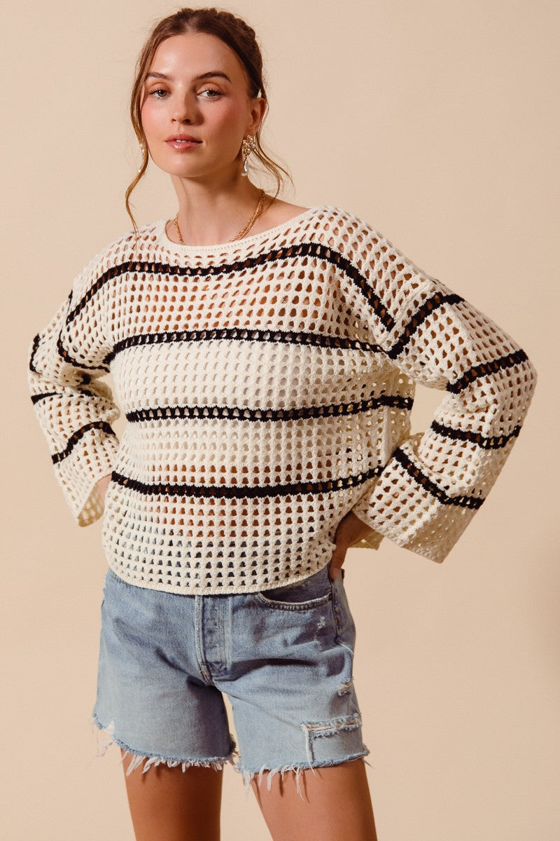 Woman wearing a white crochet top with black stripes and denim shorts on a beige background