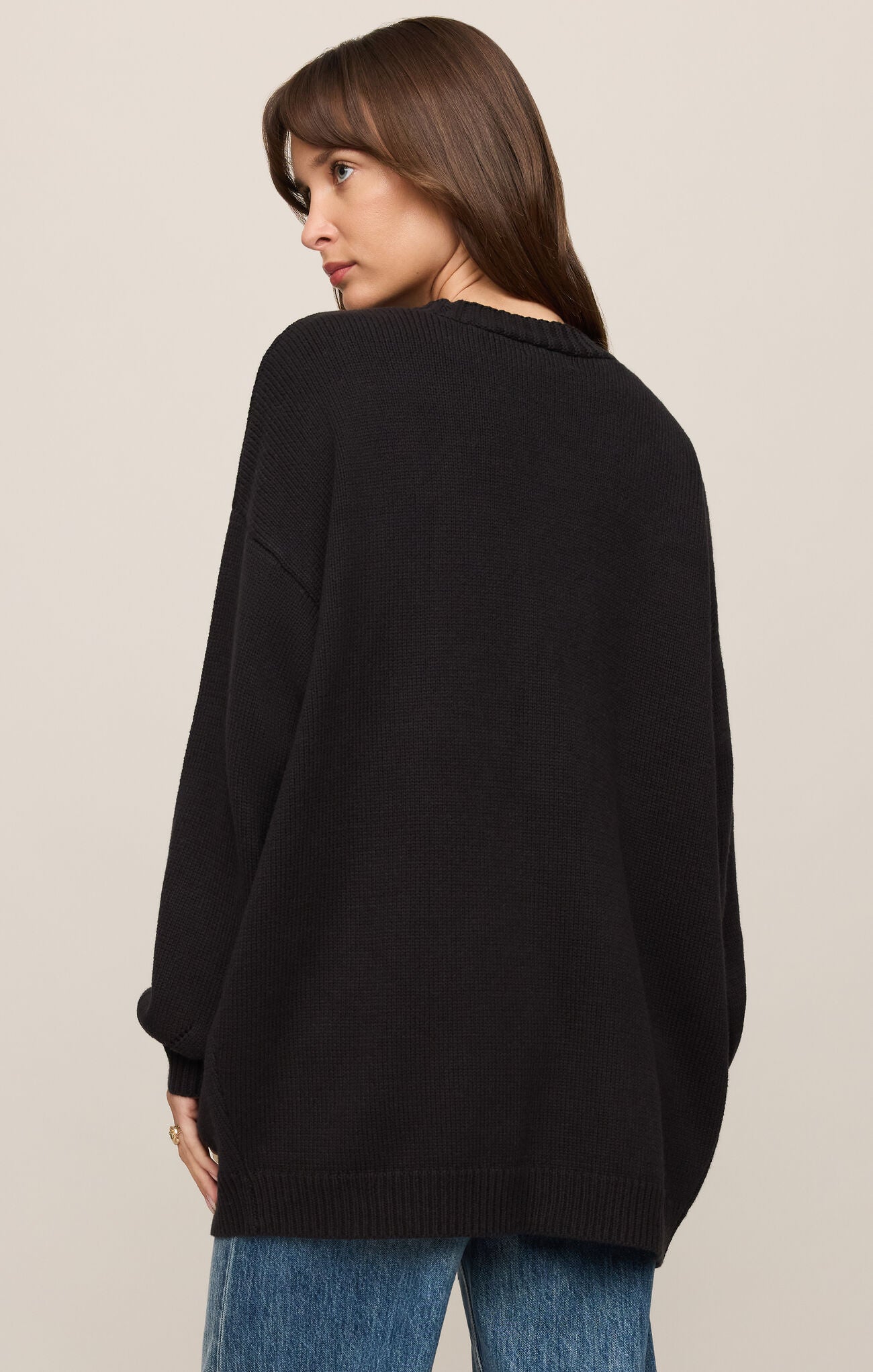 Woman wearing a black sweater and blue jeans on a beige background