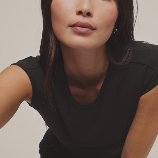 Woman wearing a black top and black pants against a beige background