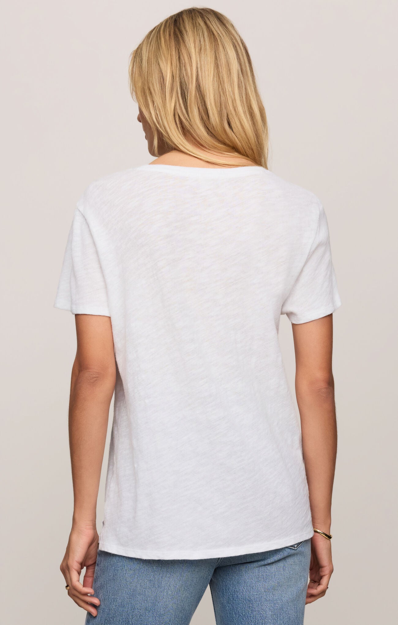 Person wearing a plain white t-shirt and blue jeans on a beige background