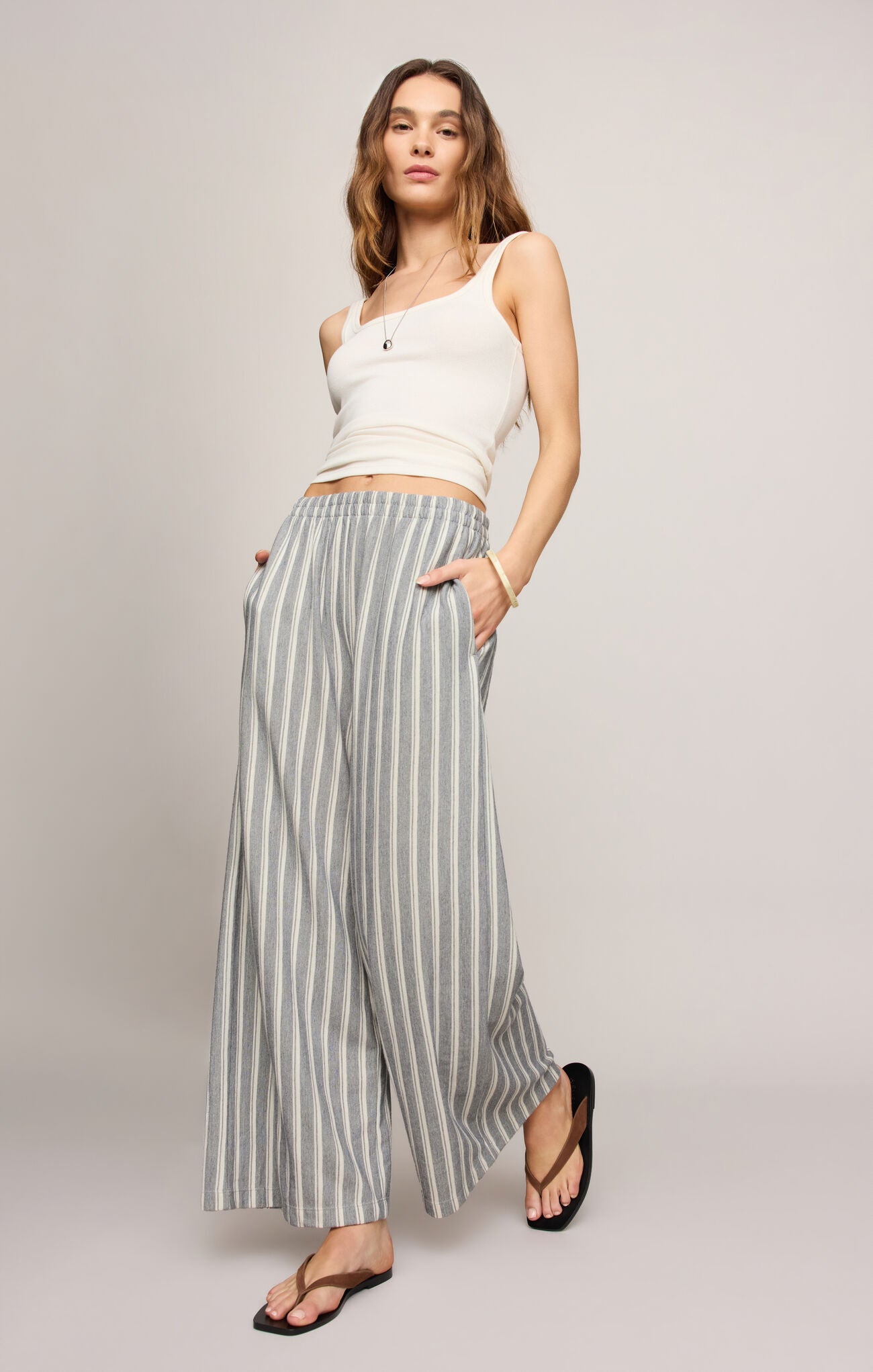 Woman wearing a white sleeveless top and striped wide-leg pants on a plain background