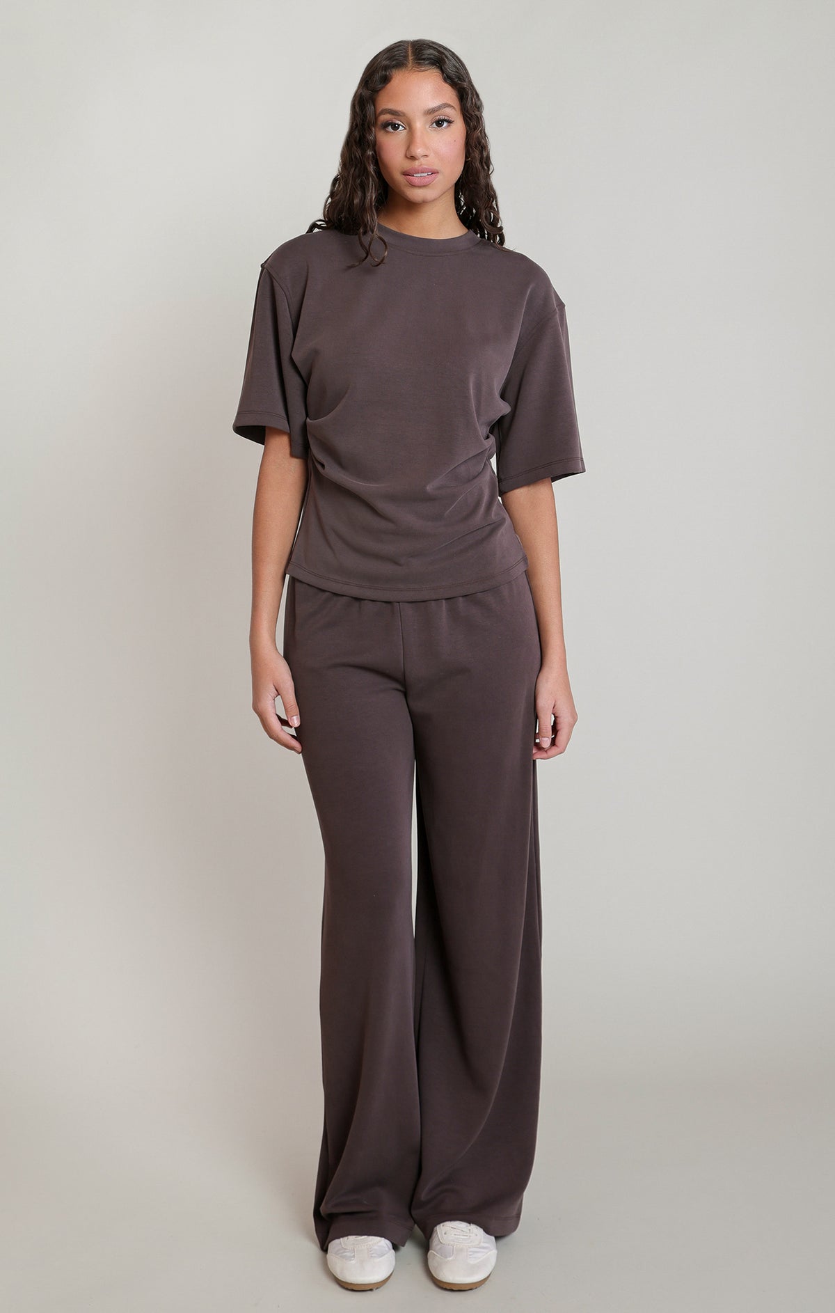 Woman wearing a brown outfit with wide-leg pants on a plain background
