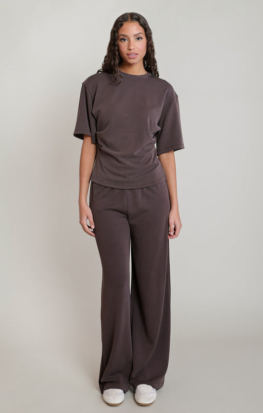 Woman wearing a brown outfit with wide-leg pants on a plain background